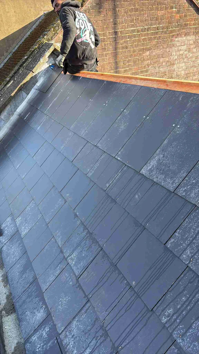 Grey roof covering beside a brick wall