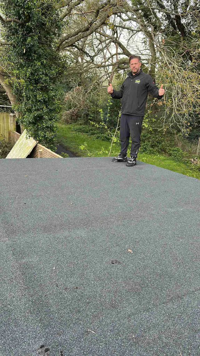 Roofing work on a flat roof beside garden trees
