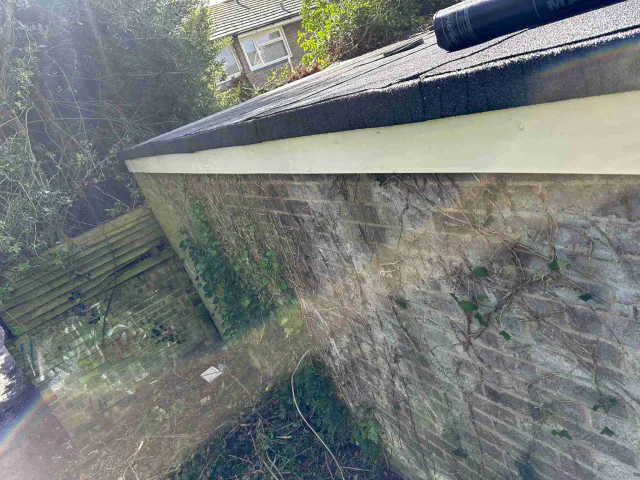 Garage roof edge and fascia beside a brick wall